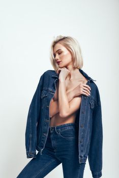 Great look. Sexy young woman in jeans wear keeping eyes closed while standing against grey background in studio. Denim clothes. Fashion concept. Beauty