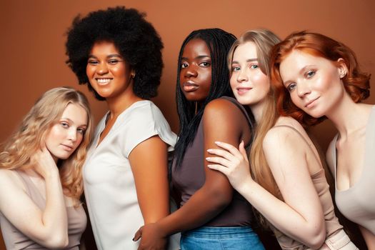 young pretty african and caucasian women posing cheerful together on brown background, lifestyle diverse nationality people concept closeup