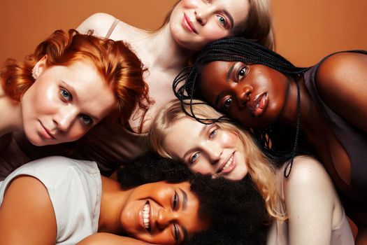 young pretty african and caucasian women posing cheerful together on brown background, lifestyle diverse nationality people concept close up