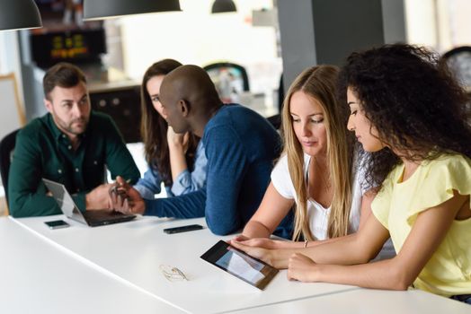 Five young people studying with tablet and laptop computer on white desk. Beautiful women and men working together wearing casual clothes. Multi-ethnic group.