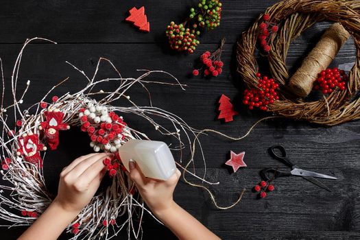 Christmas background. Top view of female hands make a Christmas wreath. Packed gifts and scrolls, spruce branches and tools on wooden table. Workplace for preparing handmade decorations.