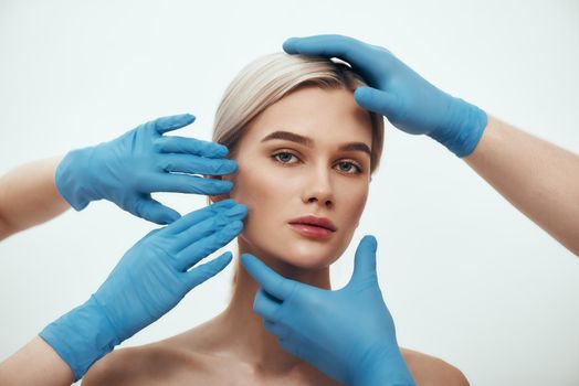 Facial surgery. Beautiful blonde woman waiting for facial surgery while surgeons in blue medical gloves examining her face. Plastic surgery concept. Healthcare. Beauty concept.