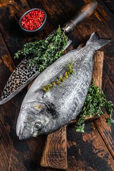 Raw dorado fish on a cutting board with knife. Dark wooden background. Top view.