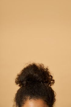 Studio shot of young mixed race woman with highly raised dark curly hair posing isolated over beige background. Vertical shot