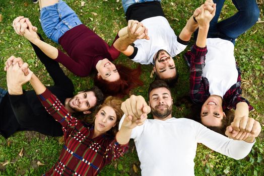 Women and men laying on grass wearing casual clothes. Group of young people together outdoors in urban park.