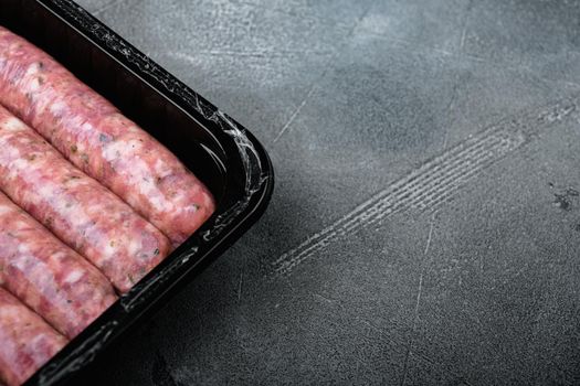 Uncooked meat sausages in plastic pack set, on gray stone table background, with copy space for text