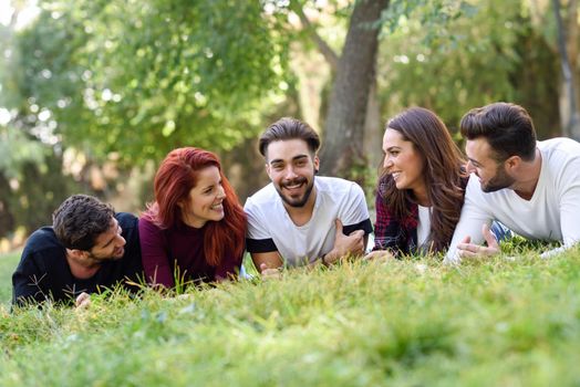 Group of young people together outdoors in urban park. Women and men laying on grass wearing casual clothes.