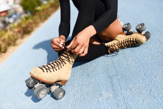Close-up of black girl sitting on bike line and puts on skates. Unrecognizable woman. Rollerblading concept
