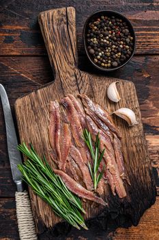 Anchovies pickled fish fillet on a wooden board. Dark wooden background. Top view.