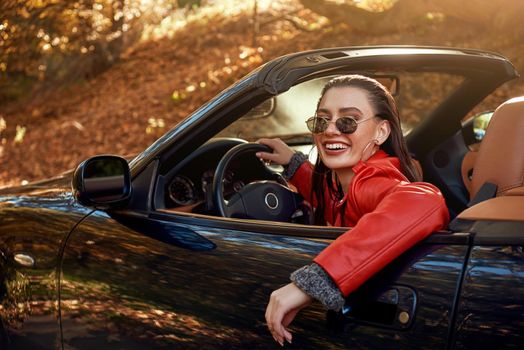 Beautiful girl in the roofless car. Autumn season, red coat and jeans, stylish sunglasses on head