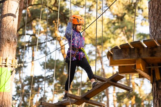 the girl in the orange helmet in the adventure Park holds on to the ropes