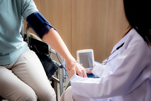 Doctor woman in uniform measuring blood pressure with patient elderly for checkup pulse health and examination at the hospital, physician and healthcare, diversity of ethnicity, medical concept.