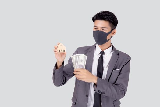 Young asian businessman in face mask holding money dollar and home isolated on white background, pandemic and crisis of economic, business man and investment property during disease covid-19.