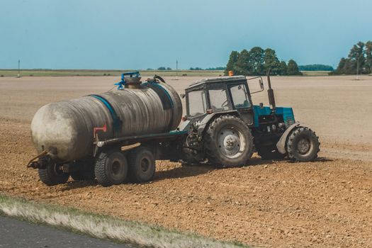 Tractor with a barrel of fertilizer in the field. Agricultural equipment and industrial work on the farm.