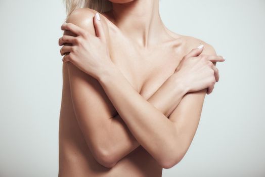 Perfection of human body. Cropped photo of sexy slim woman covering her breast with her hands while standing against grey background. Nude portrait. Sensuality. Beauty concept