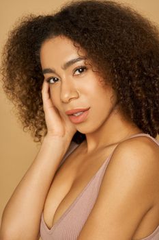 Portrait of gorgeous mixed race young woman with curly hair looking at camera while posing, standing isolated over light background. Natural beauty, skincare concept