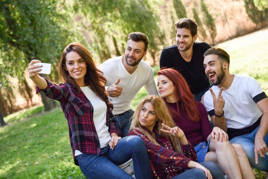 Group of friends taking selfie in urban park. Five young people wearing casual clothes.