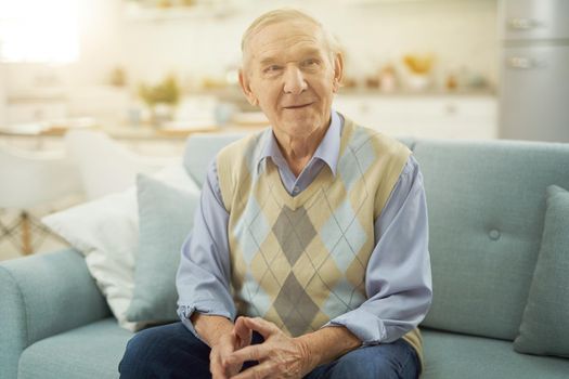 Handsome old man dressed in smart casual style sitting on couch at home. Lifestyle concept