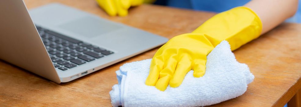 Hand of young asian woman cleaning and wipe laptop computer with disinfect and alcohol for protect pandemic covid-19 at home, girl in gloves cleaner notebook for hygiene, health care concept.