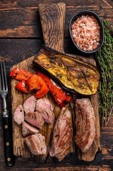 Roasted lamb tenderloin Fillet Meat steak on wooden cutting board. Dark wooden background. Top view.