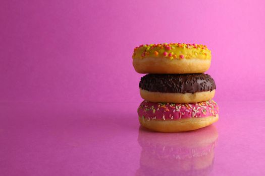 three Berliners donut pink yellow chocolate with a sprinkle on a pink background leit stack on top of each other with a copyspace.