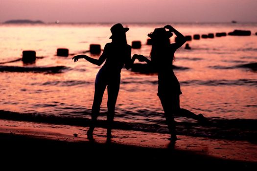 Silhouette of two young woman having fun on the sea beach