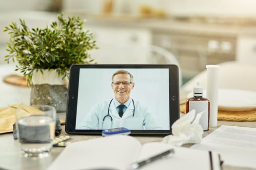 Digital tablet with an image of a medical doctor on it propped on a table full of medication