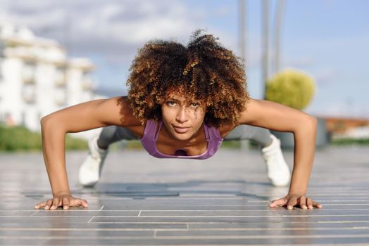 Black fit woman doing pushups on urban floor. Young female working out in the street.