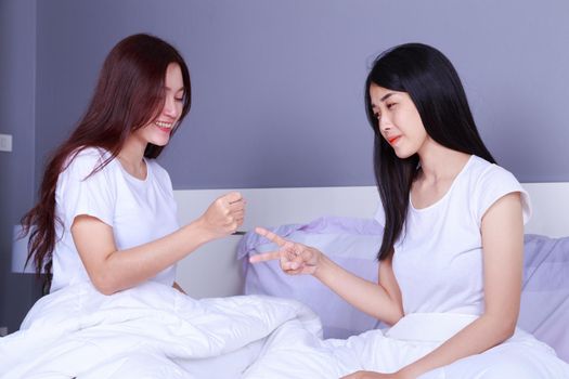 two woman playing rock paper scissors on bed in the bedroom