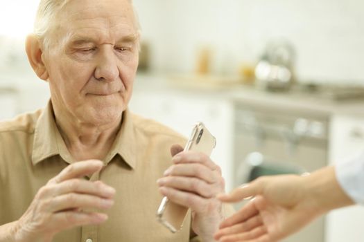 Cropped photo of elderly man looking thoughtful while holding a smartphone in his kitchen