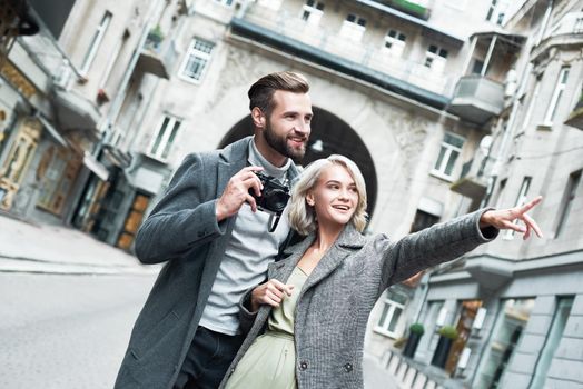 Romantic date outdoors. Young couple standing on the city street man holding camera while woman pointing aside at beautiful view smiling happy