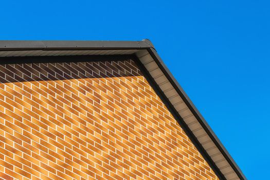 Modern house facade with brown brick wall interior against blue sky background.