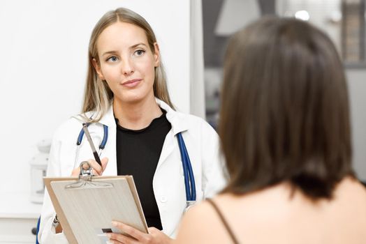 Female doctor explaining diagnosis to her patient. Brunette woman having consultation with blonde girl in medical office.