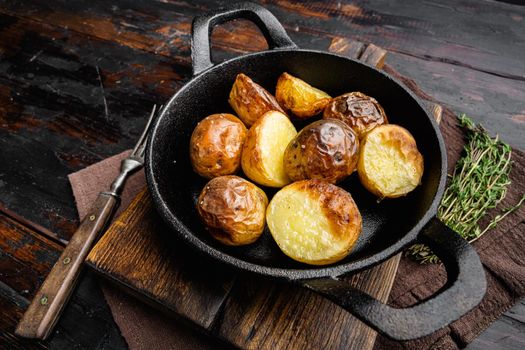 Oven baked potatoes with rosemary set, in frying cast iron pan, on old dark wooden table background