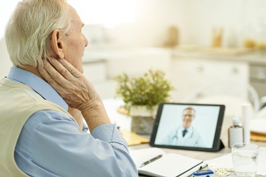 Copy space photo of aged man looking at tablet screen while having a video-calling with medical specialist