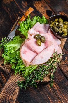 Sliced smoked ham with fresh salad and herbs. Dark wooden background. Top view.