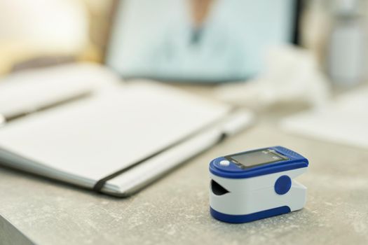 Selective focus of fingertip pulse oximeter sitting on the tabletop near an open notebook