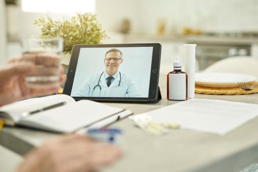Black tablet with image of a medical worker smiling while video-calling his eldelry patient