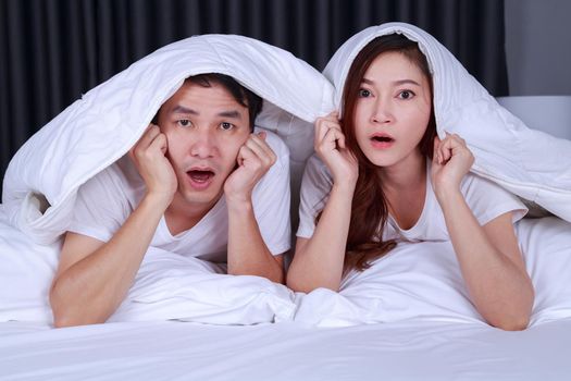 young couple watching scared movie under the blanket on bed