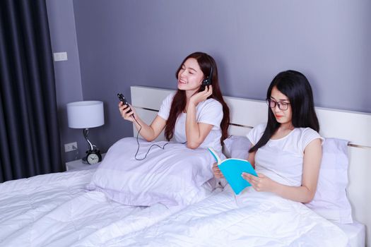 two woman reading a book and using smart phone on bed in the bedroom