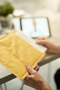 Cropped photo of person opening a yellow postal envelope with a digital tablet in the background