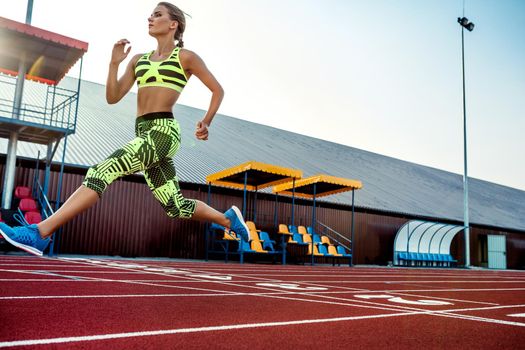 Young, beautiful girl athlete in sportswear runs along the treadmill. Sport background. Outdoor stadium