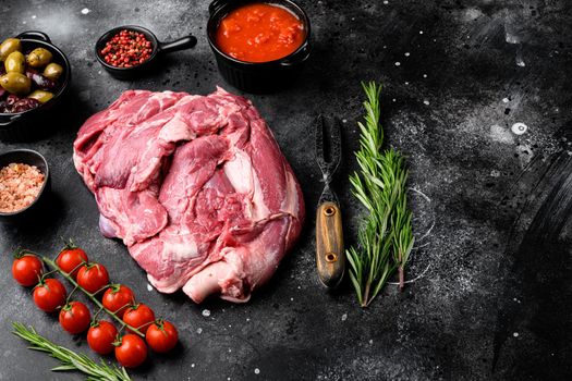 Raw lamb shoulder meat ready for baking set, with ingredients and herbs, on black dark stone table background, with copy space for text