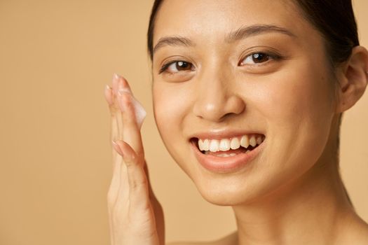 Studio portrait of lovely young woman smiling at camera while applying gentle foam facial cleanser. Beauty products and skin care concept