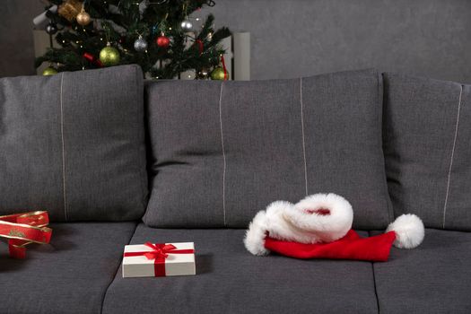 Santa hat and open gift box on gray couch. End of New Years Eve.