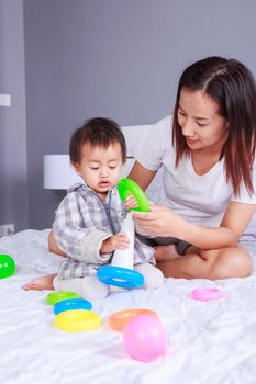 baby playing toys with mother on bed at home