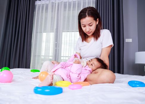 baby drinking a milk from bottle with mother on a bed