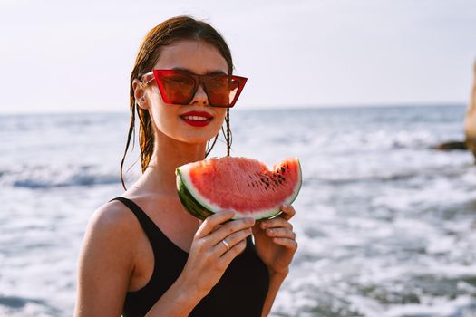 cheerful woman in sunglasses eating watermelon by the ocean. High quality photo