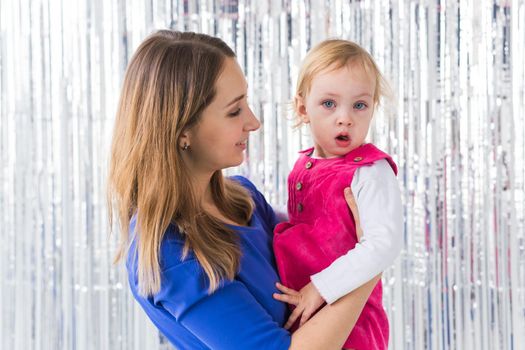 Childhood, holidays and family concept - Mother kissing baby daughter on shiny background. Close-up.