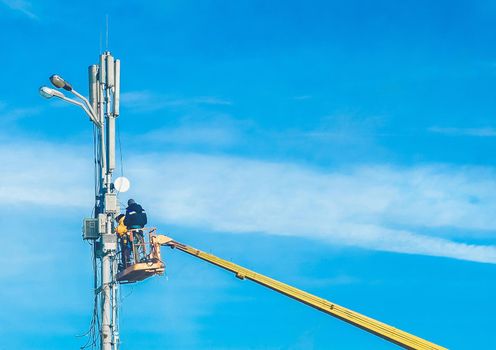 Two men, raised on a crane, will repair the power line support against the blue sky. Dangerous profession, selective focus.